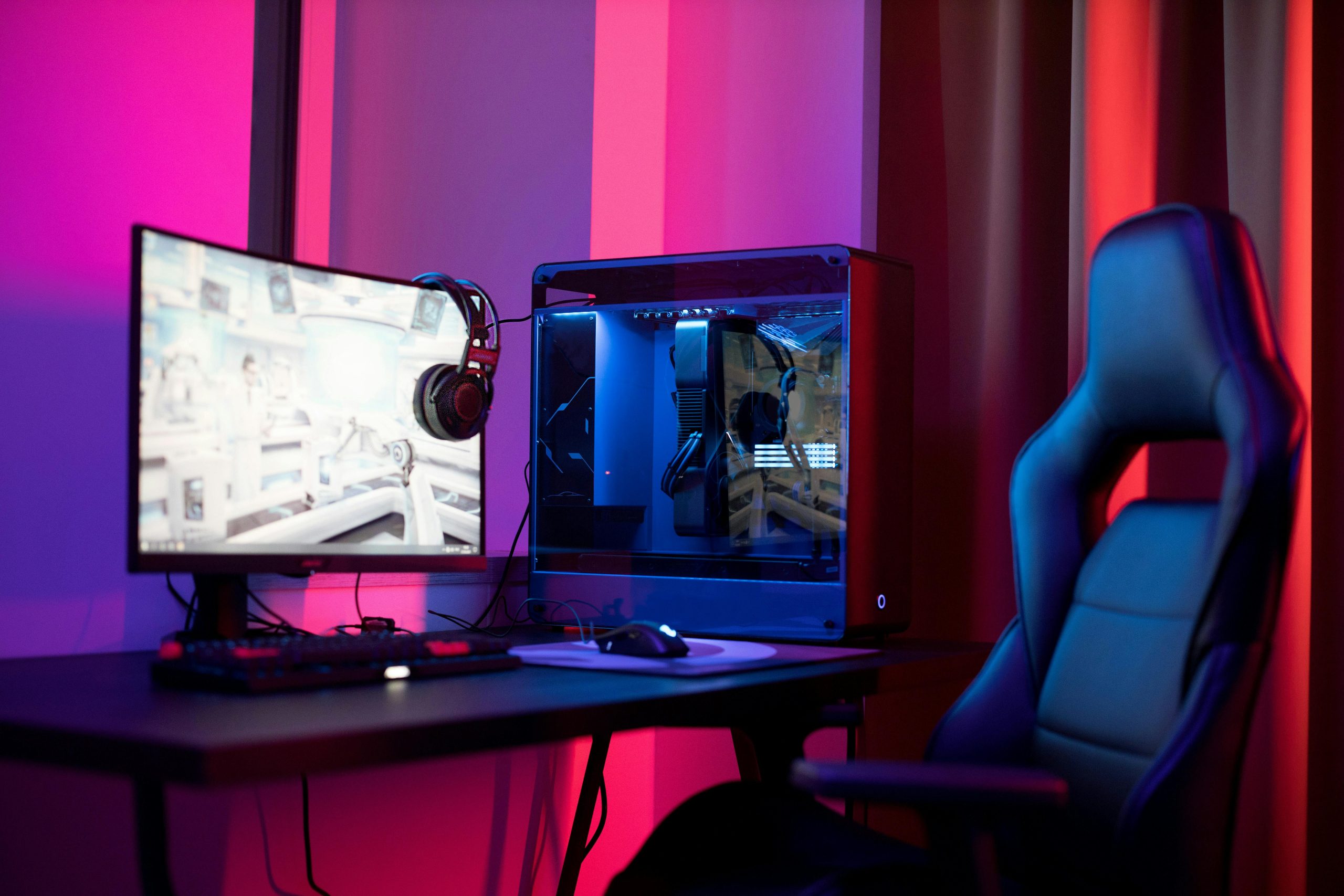 A sleek gaming setup featuring a high-end PC, widescreen monitor, and ergonomic chair lit by neon lights.